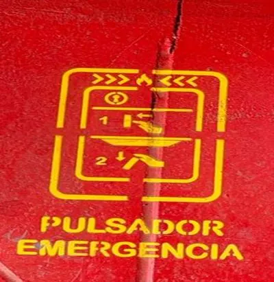 Señalización amarilla de pulsador de emergencia sobre superficie roja