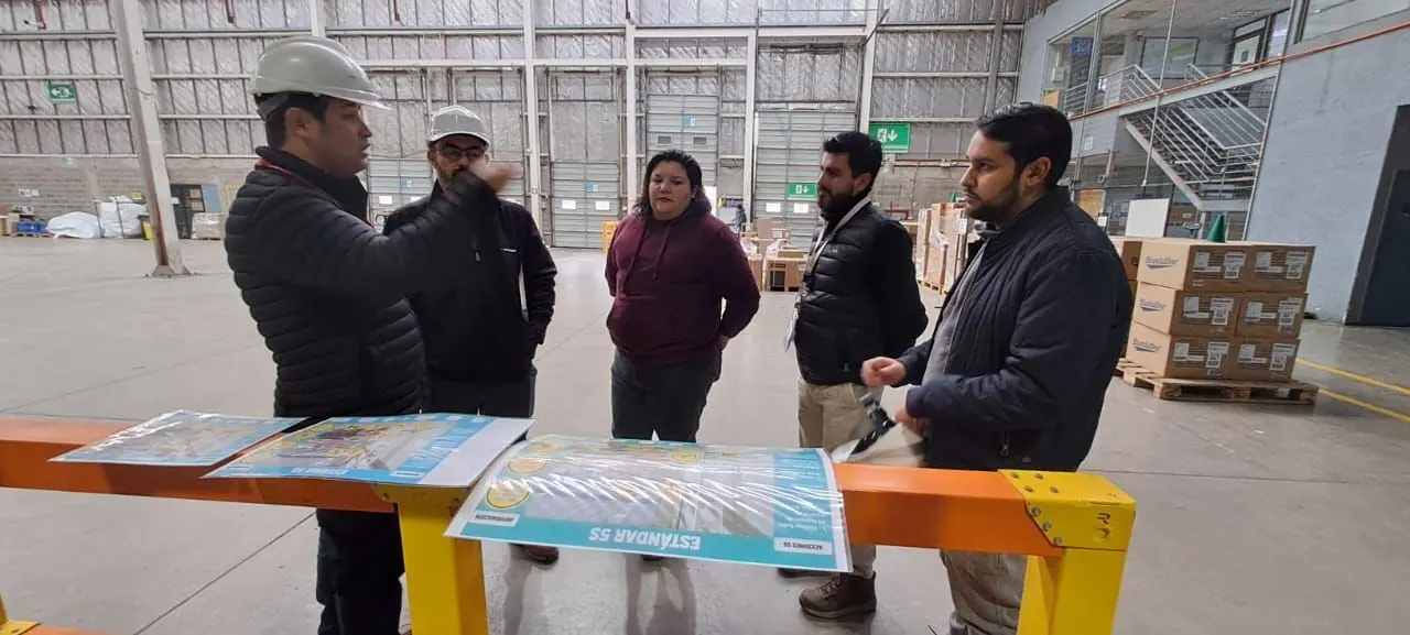 Equipo revisando en terreno láminas impresas del Estándar 5S sobre una viga amarilla, en un galpón industrial
